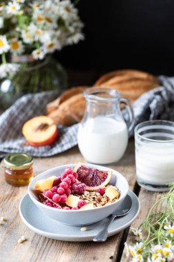 Çilek ve meyve ve bal ve ahşap bir masada süt veya yoğurt bir bardak ile Granola kahvaltı. Papatya buketi. Rustik