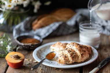 Taze ekmek ve süt ve şeftali veya kayısı reçeli ile kruvasan ahşap bir masa üzerinde. Papatya buketi. Rustik