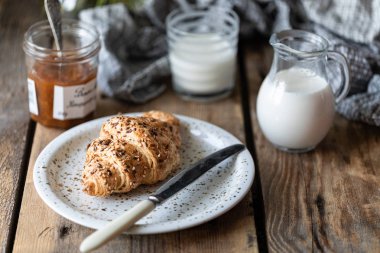 Taze ekmek ve süt ve şeftali veya kayısı reçeli ile kruvasan ahşap bir masa üzerinde. Papatya buketi. Rustik