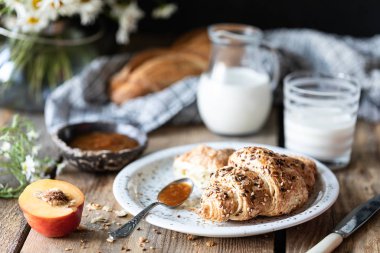 Taze ekmek ve süt ve şeftali veya kayısı reçeli ile kruvasan ahşap bir masa üzerinde. Papatya buketi. Rustik