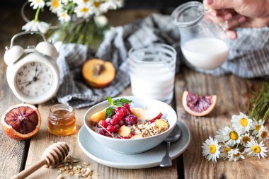 Çilek ve meyve ve bal ve ahşap bir masada süt veya yoğurt bir bardak ile Granola kahvaltı. Papatya buketi. Rustik