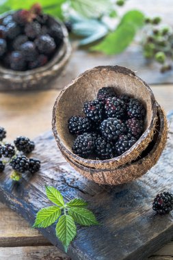 Olgun böğürtlenler tarafından doldurulmuş iki hindistan cevizi parçası eski bir tahta üzerinde.