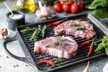 Çiğ taze et. Baharatlar, sebzeler ve otlar ile, bir ızgara tavada malzemelerle iki biftek