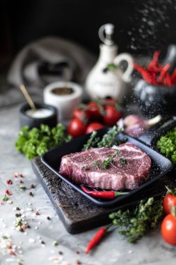 Çiğ taze et. Baharatlar, sebzeler ve otlar ile, bir ızgara tavada malzemelerle iki biftek