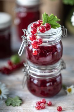 Kırmızı frenk üzümü sosu veya reçel iki cam kavanoz ve taze çilek ve çiçek ahşap bir arka plan üzerinde