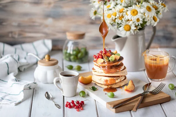 Maismehl-Pfannkuchen mit gesalzenem Karamell, serviert mit Beeren und Früchten auf weißem Holzgrund. — Stockfoto