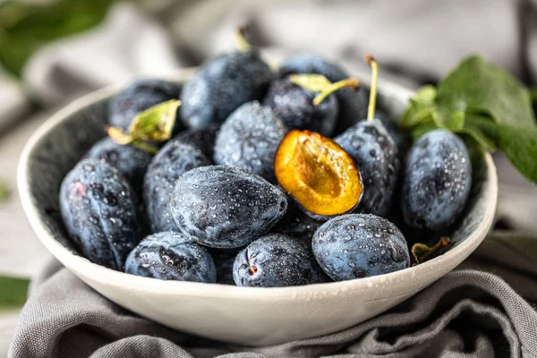 Dark blue plum in a plate on a white table.