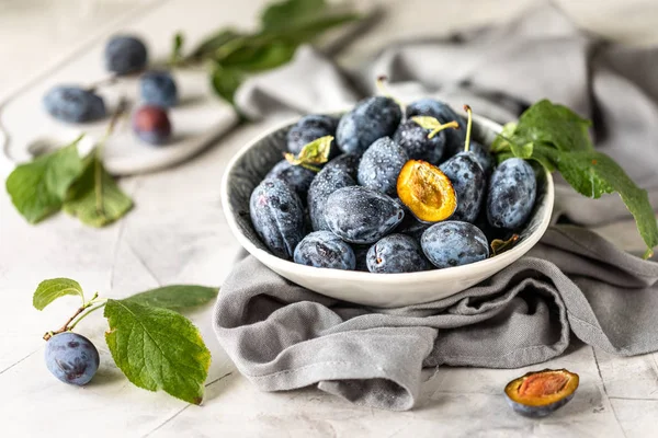 Dark blue plum in a plate on a white table.