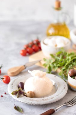 İtalyan peynirli burrata ve zeytinli mozzarella, kiraz domatesli ve roka açık arkaplanda yuvarlak beyaz bir tabakta.