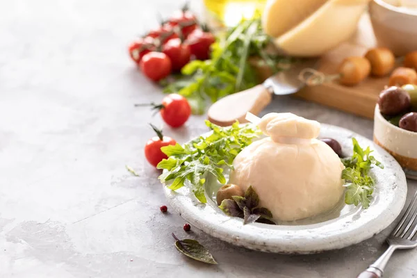 Włoskie sery burrata, mozzarella, scorocia, boccini z oliwkami, pomidory wiśniowe i rukola na okrągłym białym talerzu na jasnym tle. Przestrzeń kopiowania. — Zdjęcie stockowe