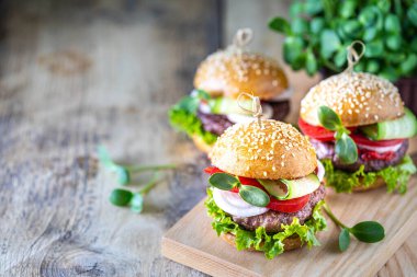 Ev yapımı hamburgerler pirzola, taze marul, domates, ahşap bir masada soğan. Fast food.