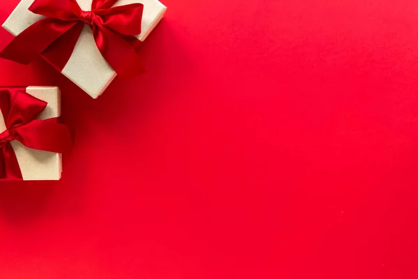 Two gift boxes with a red bow on a red background, top view with copy space.