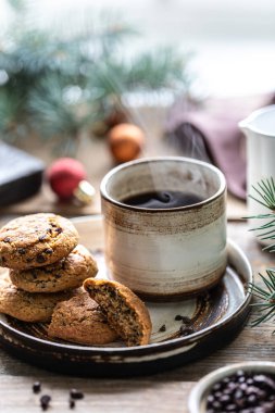 Ev yapımı fındıklı kurabiyeler ve seramik bir fincanda kahve oyuncaklarla ve Noel ağacı dallarıyla ahşap bir masada..