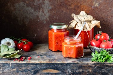 Yandaki ahşap masada ev yapımı domates soslu birkaç cam kavanoz..