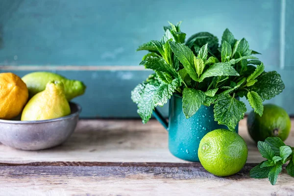 Fresh organic mint and lemon balm in a metal mug, and limes and lemons on a wooden table. Selective focus. Rustic