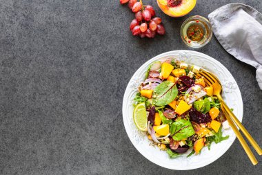 Siyah arka planda beyaz bir tabakta taze sebze salatası, roka, kırmızı soğan, kuş, nohut, şeftali ve üzüm. Üst görünüm