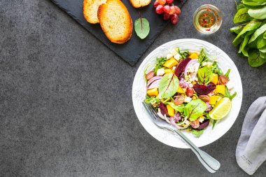 Taze sebze salatası, pancar, roka, kırmızı soğan, kuş, nohut, balkabağı ve üzümler siyah arka planda beyaz bir tabakta..