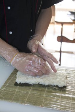 Ellerinizi kapayın ve suşi için pilavı öğütün bambu hasırında rulo yapın