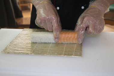 Erkek şef restoranda somonla suşi yapıyor. 