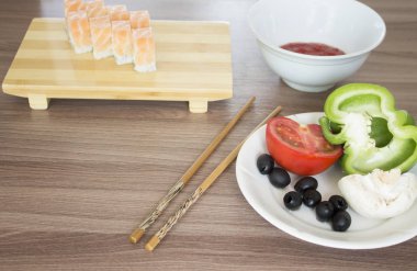 Taze suşi rulosu, sebzeler, yemek çubukları masada. 