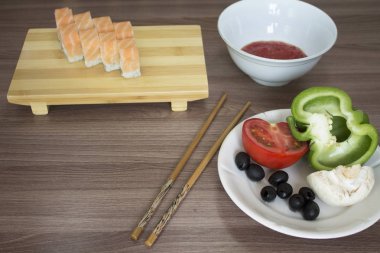 Taze suşi rulosu, sebzeler, yemek çubukları masada. 