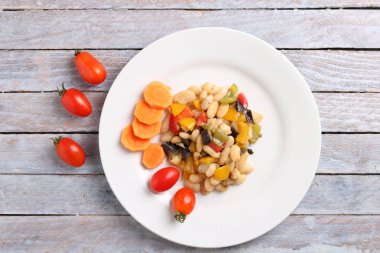 Havuç dilimleri, domatesler ve masada fasulye ve sebzeden yapılmış yemekler.