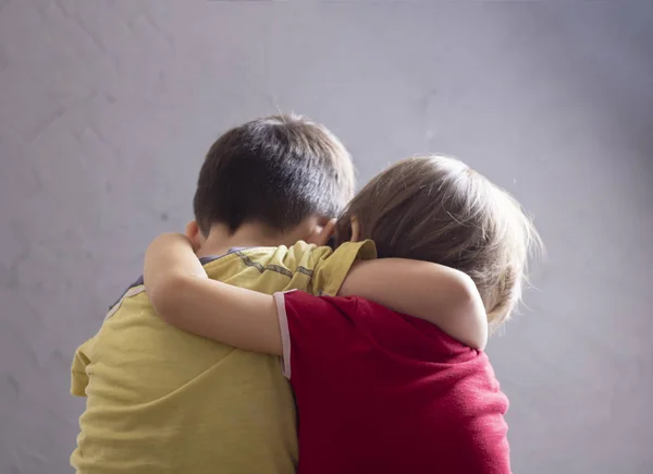 back view of brothers are hugging by the wall  of the house.