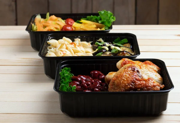 Three black food boxes with boiled beans, baked chicken wings and steamed vegetables — Stock Photo, Image