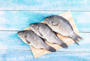 Tahta doğrama tahtasının üzerinde üç taze çiğ deniz balığı, düz yerde. Metin için yer