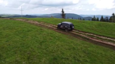 Toprak bir yolda, dağlık bir arazide siyah bir SUV sürüyor. Hava görünümü.