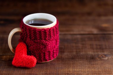 Koyu ahşap dokusuna kırmızı örülmüş bir fincan siyah çay, yakın plan.