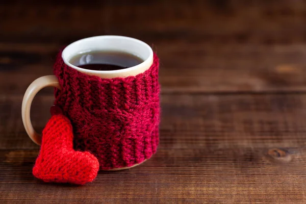 Koyu ahşap dokusuna kırmızı örülmüş bir fincan siyah çay, yakın plan.