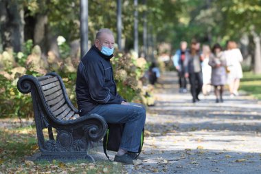Vilnius, Litvanya - 07 Ekim - 7 Ekim 2020 'de Litvanya' nın Vilnius kentinde halk parkında oturan koruyucu maskeli bilinmeyen bir adam