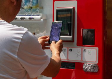 Sakallı yakışıklı hipster adam sırt çantası ile rahat kıyafetler giymiş Avrupa şehri tatil gezisi sırasında self servis satış makinesi istasyonu, otobüs biletleri satın alıyor. Işık parlaması.