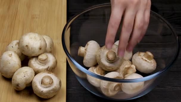 Jefe de cocina pone sus champiñones pelados en un recipiente de vidrio junto a una pila de champiñones en una tabla de cortar . — Vídeo de stock