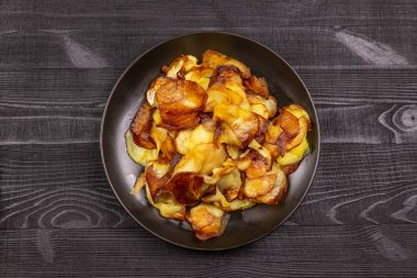 Fried homemade potato chips in a black plate on a wooden rustic background.