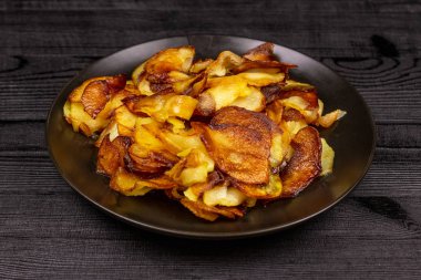 Fried homemade potato chips in a black plate on a wooden rustic background