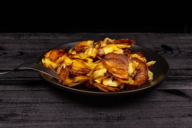 Fried homemade potato chips in a black plate on a wooden rustic background