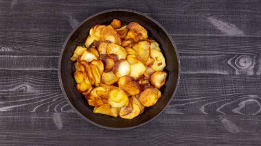 Fried homemade potato chips in a vintage antique cast-iron pan on a wooden rustic background.