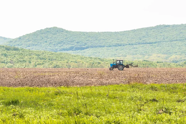 Il trattore aratura il terreno con un coltivatore rompendo zolle nei letti e preparando il campo per la semina primaverile — Foto Stock