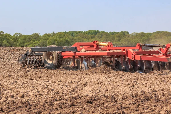 Il trattore aratura il terreno con un coltivatore rompendo zolle nei letti e preparando il campo per la semina primaverile — Foto Stock