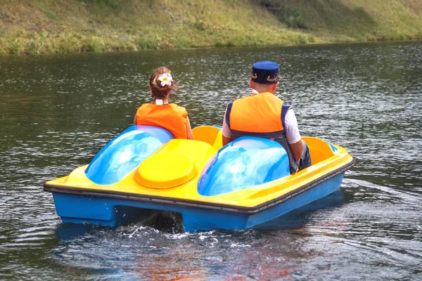 若いカップル - ロシアの女の子と伝統的な民族衣装を着た男と都市公園の池にペダルを持つカタマランの遊覧船にタタルキャップに乗る — ストック写真