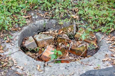 The concrete well of the city drainage system is overgrown with grass and filled with stones and mud with branches. An abandoned storm drains sump is not serviced and has problems clipart