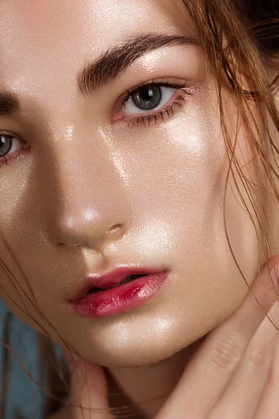 Close up beauty of a half face of a woman with wet radiant skin and big gray eyes. Fashionable natural makeup and wet facial hair. Pink lipstick with kissed lips