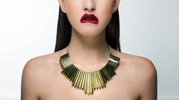 Close up glamor image of a female predator with a bite of scarlet lips. On the neck of the girl gold jewelry and sparkles on the body. Beautiful transparent skin, straight laminated hair. Spa care or cosmetology care. Beauty sexy woman