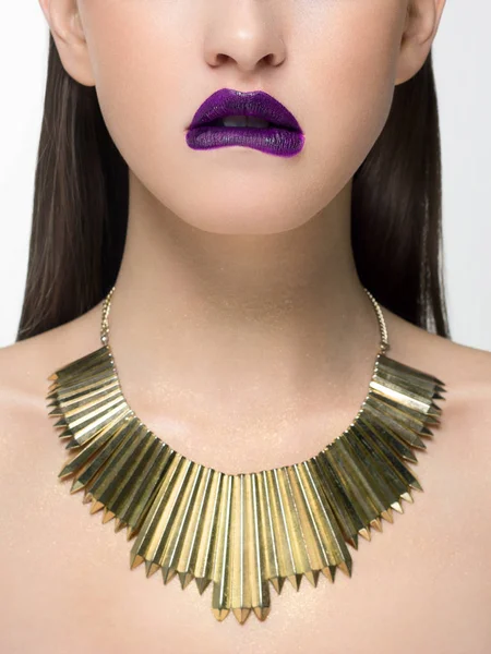 Close up glamorous image of a female predator with a bite of purple lips. On the neck are golden jewels and sparkles on the body. Beautiful transparent skin. Spa care or beauty care. Beauty sexy woman