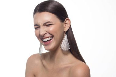 Büyük gözlü ve siyah kaşlı güzel bir kız, çıplak omuzlu, kameraya bakıyor ve gülümsüyor, açık renk makyajlı bir model, stüdyo arka planı, güzel bir fotoğraf, fotokopi alanı, kar beyazı bir gülümseme ve kulaklarında süslemeler.