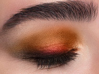 Macro shot. Close-up beauty of woman's eye. Sexy smoky eyes makeup with orange eyeshadows. Perfect strong shape of eyebrows. Make-up and Cosmetics. Great summer mood clipart