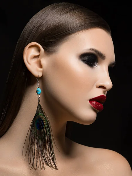 Kırmızı ruj ve moda tavus kuşu tüyü küpe ölümcül makyaj vurgulayan bir ryunette kadının muhteşem yüz özellikleri, güzelliği bir yakın çekim portre sihir görüntüye ekler.