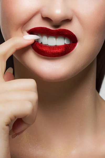 Close-up portrait of the lower half of woman\'s face with a malicious grin. He picks a long fingernail in his teeth. Beautiful full lips with a trendy lipstick wine tint. Dental smile. Teeth whitening